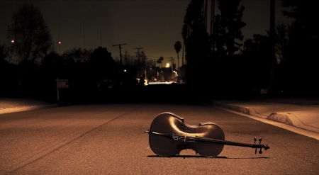 At night, a cello resting on the ground of a street.